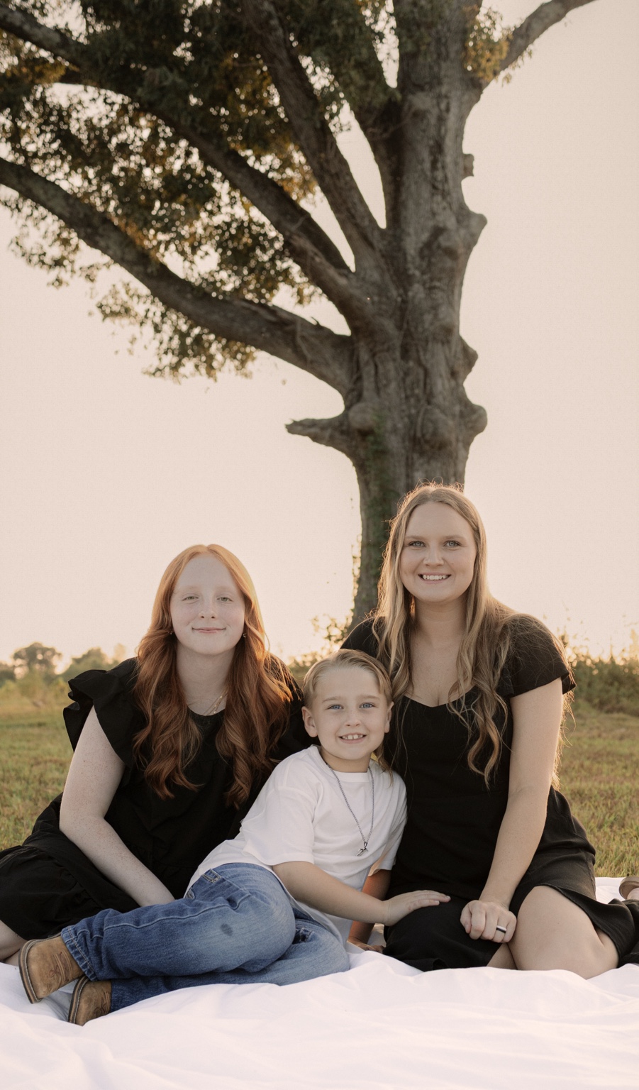 A mother and children sitting beneath a tree at sunset